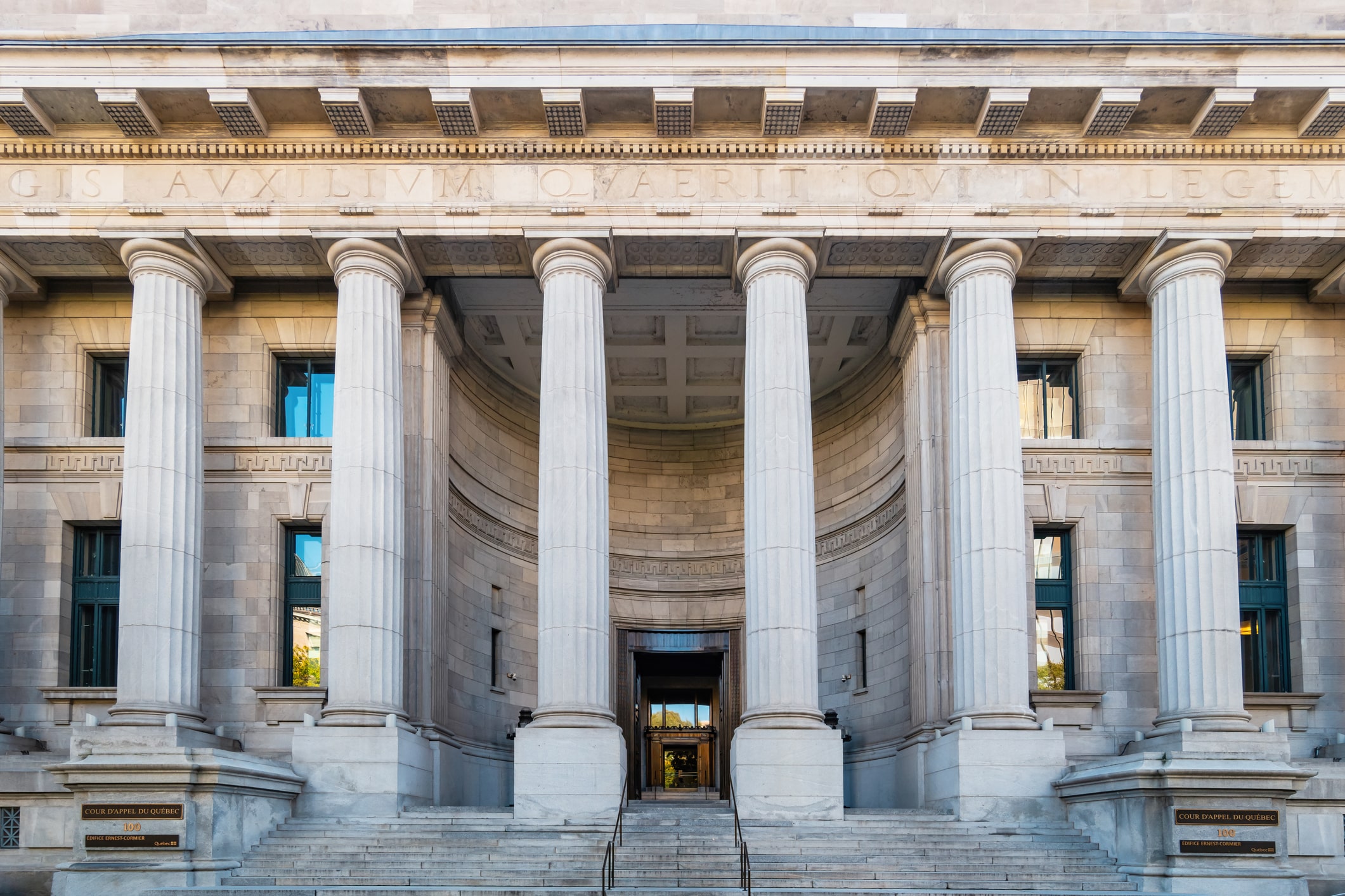 A neoclassical building with tall stone columns supporting a portico, wide steps leading to the entrance, and a Latin inscription carved above the columns on the facade.