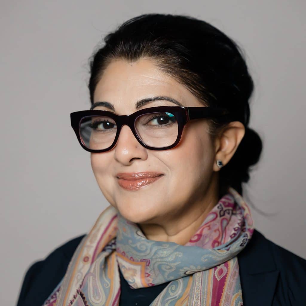 Headshot of a smiling woman wearing dark-rimmed glasses and a patterned scarf.