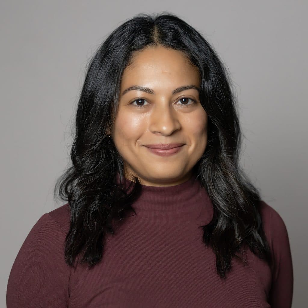 A woman with dark hair and a maroon mock-neck top smiles at the camera.
