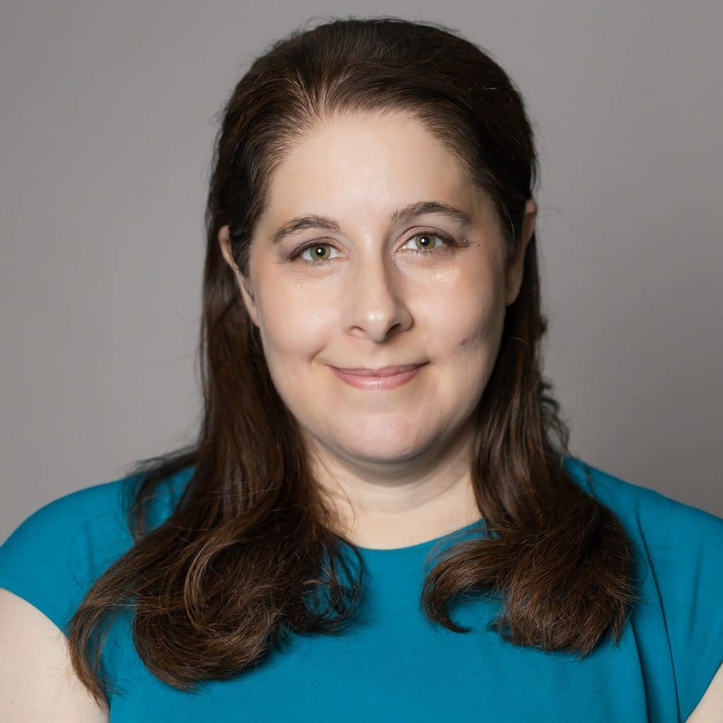 A woman with shoulder-length brown hair wearing a teal top smiles at the camera.