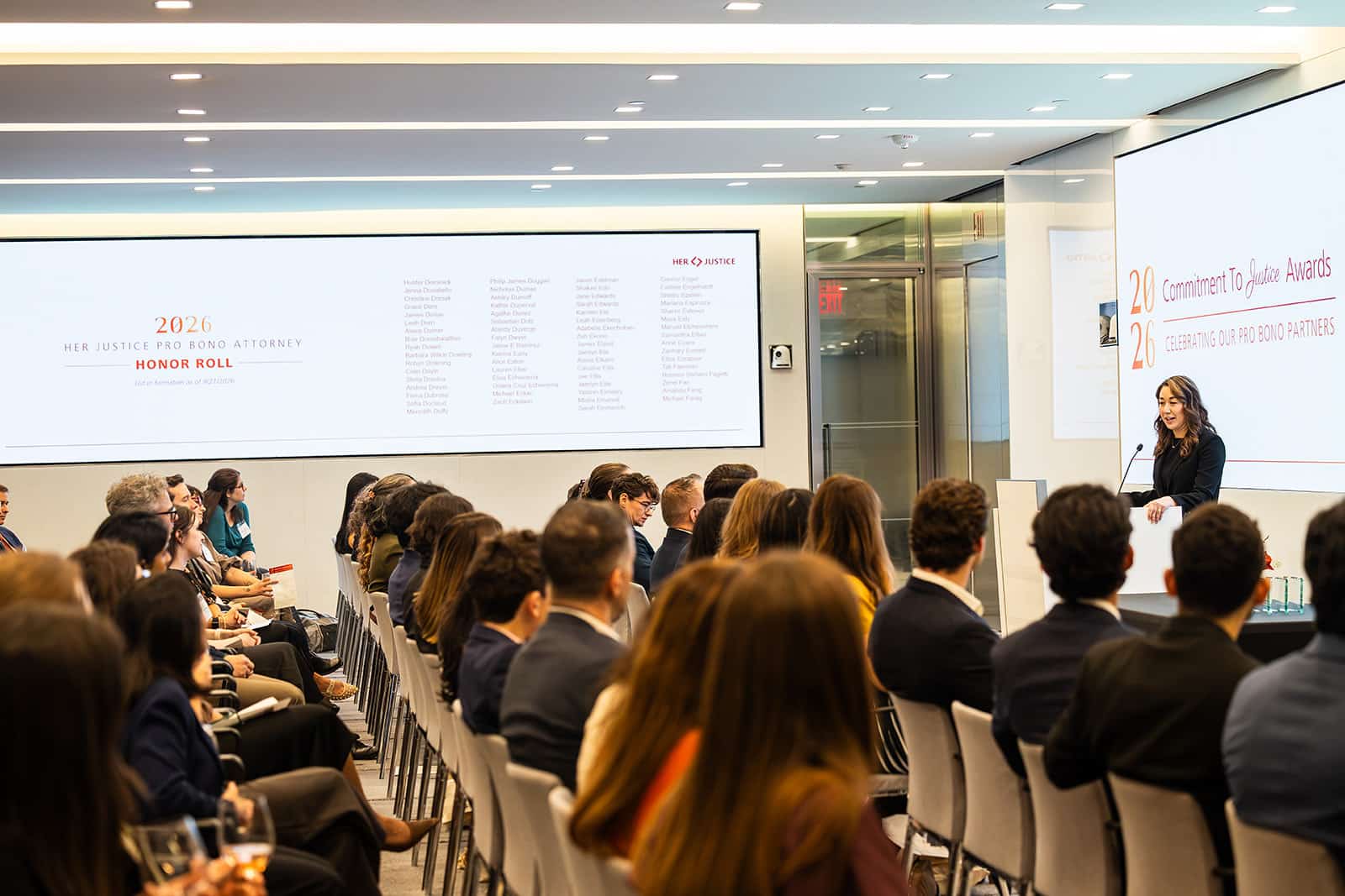 A woman speaks at a podium in front of an audience during the 2026 Her Justice Pro Bono Attorney Honor Roll ceremony.