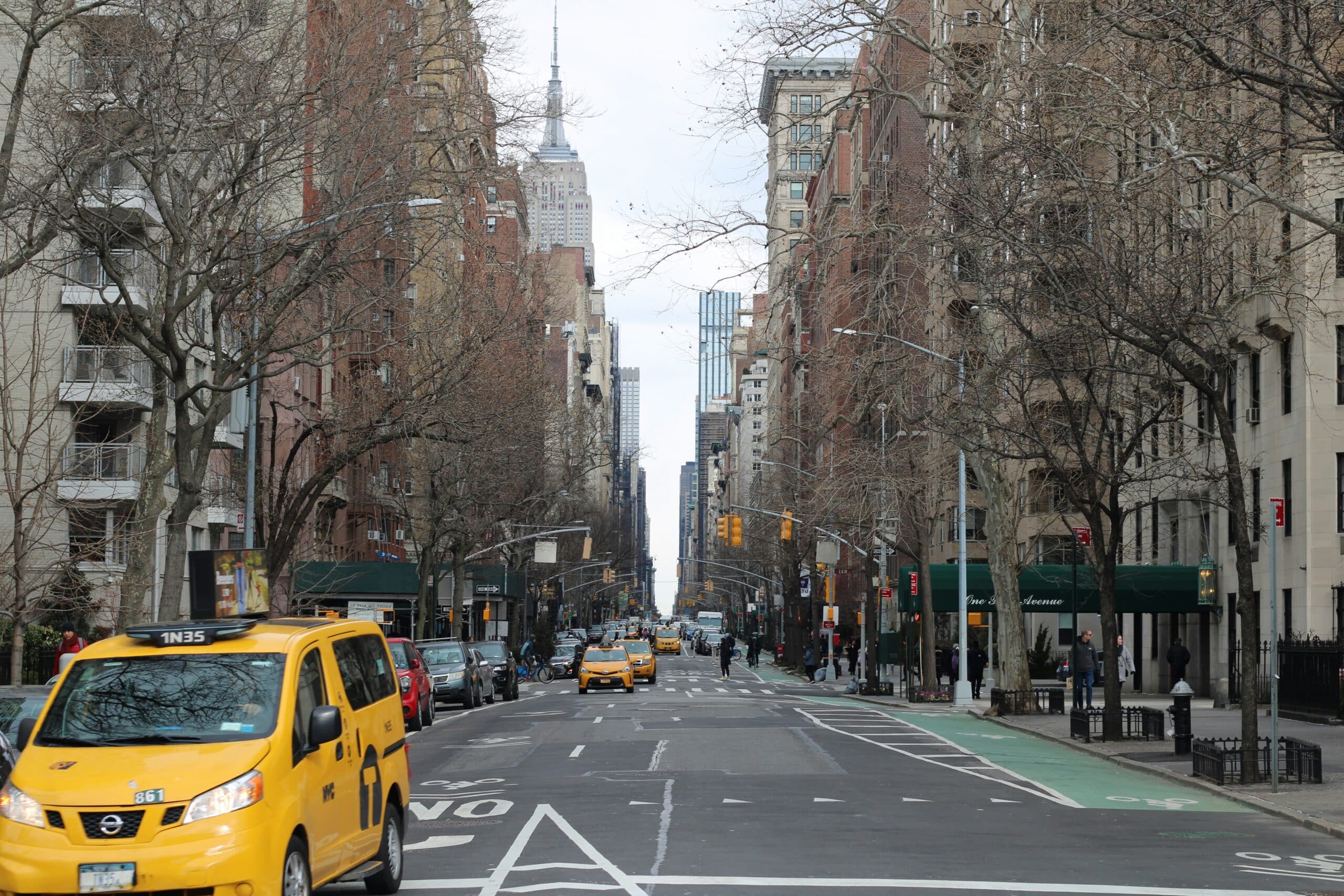 A view down a New York City avenue with yellow taxis in the street and the Empire State Building visible in the distance.
